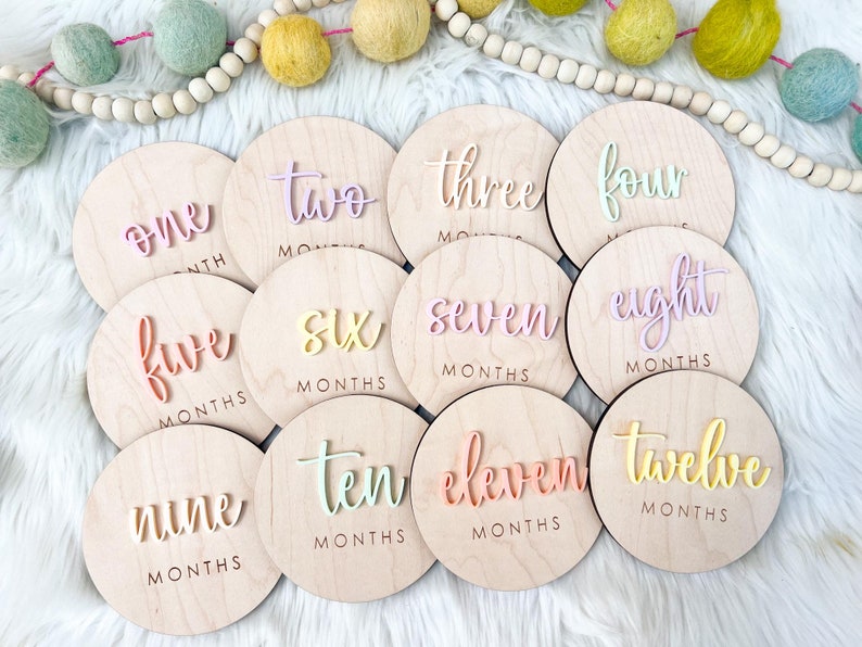 May include: Twelve wooden circles with pastel colored numbers and the word "months" written below each number. The numbers range from one to twelve.