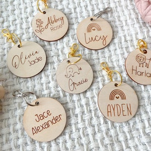 May include: Seven wooden keychains with gold rings and clips. Each keychain has a different design and name, including a flower, rainbow, elephant, lion, and more.