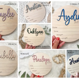 K&ouml;nnte beinhalten: Eine Sammlung personalisierter Baby-Ank&uuml;ndigungsschilder aus Holz. Jedes runde Schild zeigt einen Namen in einer kontrastierenden Farbe mit Platz zur Aufzeichnung von Geburtsdaten. Farben: Lavendel, Wintergrau, Kobaltblau, Dunkelgr&uuml;n, Pfirsich, Malve und Marine.