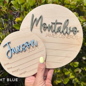 Two wooden round name plaque showing in different sizess.  Smal sign is 5" showing light blue 3D name and the bigger one is 6" showing 3D name in color sage.