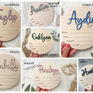 A collection of wooden baby announcement signs. Each round sign features the baby's name in a contrasting color, with space to record birth details.