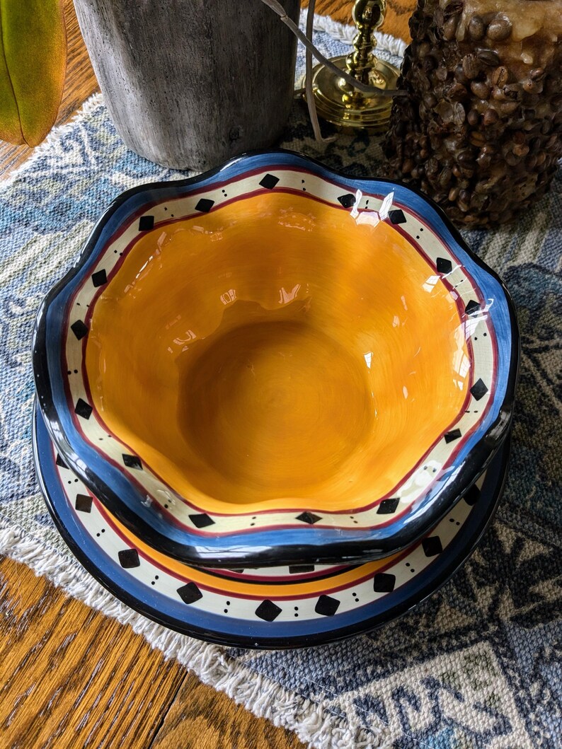 May include: A yellow ceramic bowl with a blue, black, and white rim. The bowl is sitting on a matching plate with a scalloped edge.