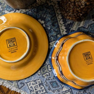 May include: Two yellow ceramic plates with blue and white trim. The bottom of each plate has a label that reads "Tabletops Gallery" and "Argentina".