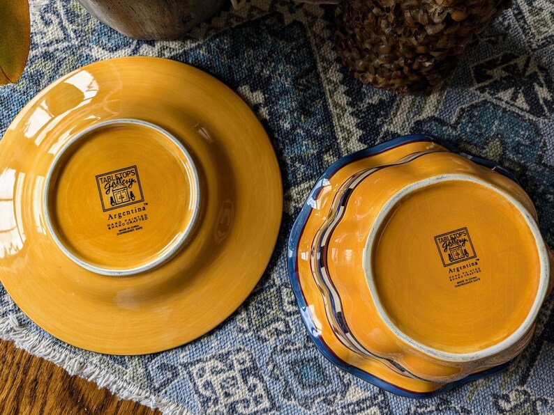 May include: Two yellow ceramic plates with blue and white trim. The bottom of each plate has a label that reads "Tabletops Gallery" and "Argentina".