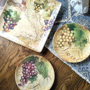 May include: A set of decorative plates with a wine theme. The plates feature images of grapes and grape leaves. One plate is square and has a map of Italy. The other two plates are round and have the word "Swirl" and "Lip" written on them.