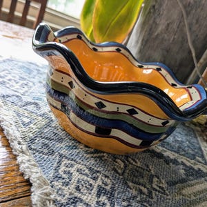 May include: A yellow ceramic bowl with a wavy rim and a black, blue, green, and white geometric design.