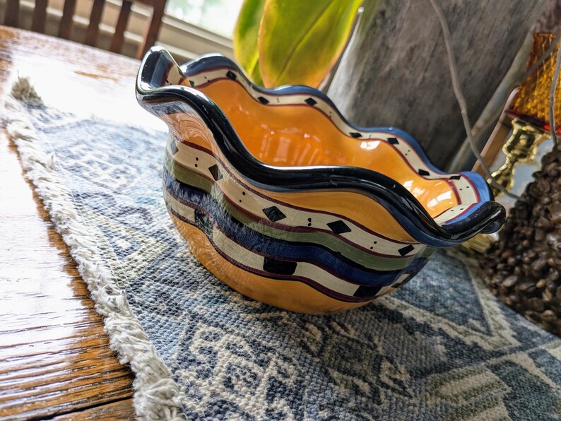 May include: A yellow ceramic bowl with a wavy rim and a black, blue, green, and white geometric design.