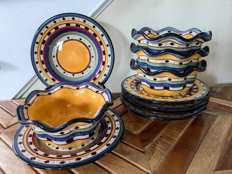 May include: Set of four colorful ceramic bowls with scalloped edges and a matching plate. The bowls and plate feature a multi-colored design with black, yellow, blue, green, and red accents.
