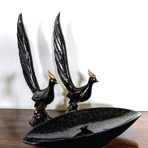 May include: Two black bird figurines with gold accents and a matching black dish. The birds have detailed feather designs and stand upright. The dish is oval-shaped and has a speckled gold pattern.