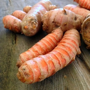 May include: Close-up of several orange turmeric roots with a knobby, fibrous texture. The roots are arranged on a wooden surface.