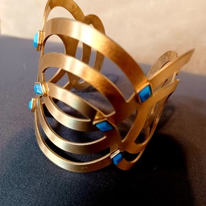 May include: Gold-toned metal bracelet with a geometric design and blue gemstone accents.