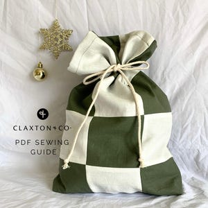 May include: A green and white checkered fabric gift bag with a white drawstring. The bag is sitting on a white surface.