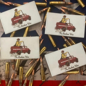 May include: Four white patches with red and black illustrations of a person driving a red fire truck. Each patch has the text "The Brothers Wax" printed on it. The patches are surrounded by gold-colored bullet casings.