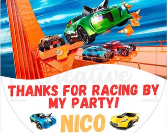 May include: A round, white thank you sticker with a red border. The sticker features a cartoon race car track with several toy cars, including a green car flying through the air. The text "Thanks for racing by my party! Nico" is printed in red, white, and orange.