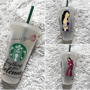 May include: A translucent plastic cold cup with a lid and dark green straw. The cup features a green Starbucks logo, the text "Anything for Selenas" and "Como La Flor", a red rose graphic, and illustrations of Selena in a purple top and a maroon outfit.