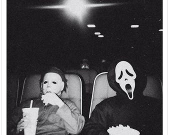 May include: Black and white sticker featuring two figures in a movie theater. One figure wears a Michael Myers mask and holds a drink. The other figure wears a Ghostface mask and holds popcorn. The background is dark.