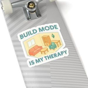 May include: A sticker with a cartoon image of a room with furniture, including a sofa, armchair, and table. The text "BUILD MODE IS MY THERAPY" is displayed in a white font with a blue outline.