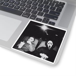 May include: Black and white sticker featuring a movie scene with two characters in costume. One character is wearing a white mask and holding a drink. The other character is wearing a Scream mask and holding popcorn.