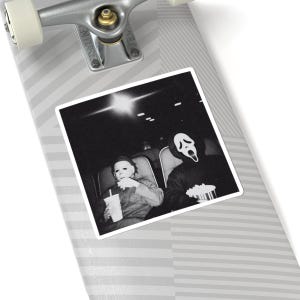 May include: Black and white sticker featuring a movie theater scene with two figures in costume. One figure wears a Michael Myers mask and holds a drink, while the other wears a Ghostface mask and holds popcorn. The sticker is placed on a skateboard.
