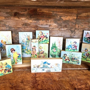 May include: A collection of 14 wooden blocks, each featuring a vintage illustration of children playing in a spring setting. The blocks are painted in pastel colors and feature details like flowers, bunnies, and birds.
