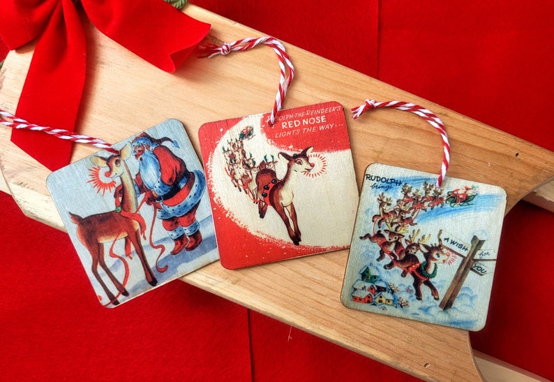 May include: Three vintage Christmas ornaments featuring Rudolph the Red-Nosed Reindeer. The first ornament shows Rudolph with Santa Claus, the second ornament shows Rudolph with the text "Rudolph the Red-Nosed Reindeer Lights the Way...", and the third ornament shows Rudolph with the text "Rudolph's Friends".