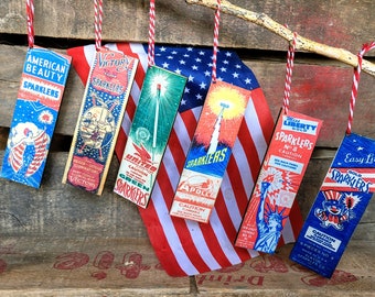 May include: Six vintage-style sparkler boxes with red, white, and blue designs. The boxes are labeled with names like "American Beauty", "Victory", "United Green", "Apollo", "Miss Liberty Gold", and "Easy Lite Gold".
