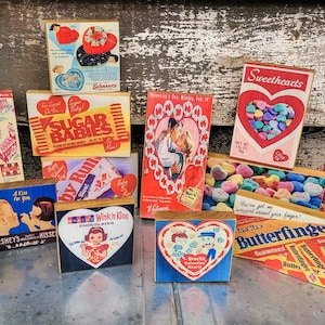 May include: A collection of vintage Valentine's Day themed wooden blocks featuring candy and chocolate brands like Sugar Babies, Hershey's Kisses, Butterfinger, and Wink in Kiss. The blocks are decorated with hearts, candy, and other Valentine's Day imagery.