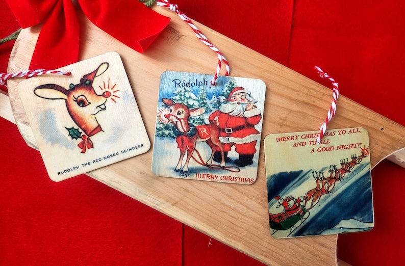 May include: Three vintage Christmas ornaments featuring Rudolph the Red-Nosed Reindeer. The first ornament shows Rudolph's face with his red nose glowing. The second ornament shows Rudolph pulling Santa's sleigh with the text "Rudolph says Merry Christmas". The third ornament shows Santa's sleigh flying through the air with reindeer and the text "Merry Christmas to all and to all a good night!"