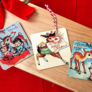 May include: Three vintage Christmas ornaments featuring Rudolph the Red-Nosed Reindeer. The ornaments are made of wood and have a rustic look. The first ornament features Rudolph with a red nose and antlers, pulling a sleigh with a green bag that says "Rudolph". The second ornament features Rudolph with a red nose and antlers, playing music with two children. The third ornament features Rudolph with a red nose and antlers, standing next to a snowman.