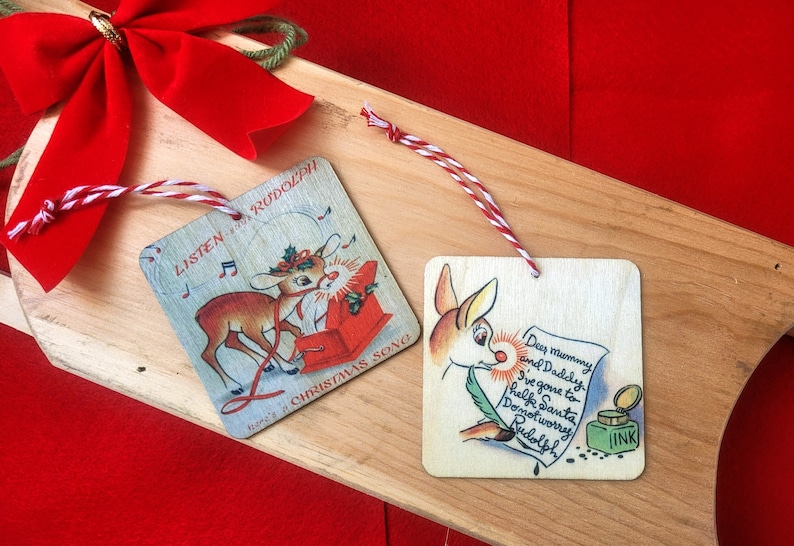 May include: Two wooden Christmas ornaments featuring a cartoon reindeer. One ornament shows the reindeer pulling a red sled with the text "Listen to Rudolph's Christmas Song". The other ornament shows the reindeer writing a letter with the text "Dear Mummy and Daddy, I've gone to help Santa. Don't worry, Rudolph."