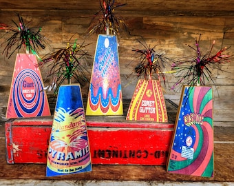 May include: Five vintage firework cone displays with colorful labels and black and silver tinsel. The labels include the names "Giant", "Conic Fountain", "Comet Glitter", "Standard Pyramid", and "Cosmos".