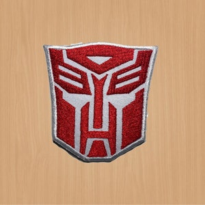 Könnte beinhalten: Roter und weißer gestickter Aufnäher mit dem Transformers-Logo. Das Logo ist ein stilisiertes Robotergesicht mit rotem Hintergrund und weißen Details.