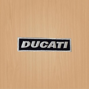 Può includere: Una toppa ricamata in bianco e nero con la parola "DUCATI" in lettere bianche.