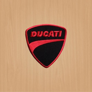 Pode incluir: Etiqueta bordada vermelha e preta com a palavra "DUCATI" em uma fonte cursiva.