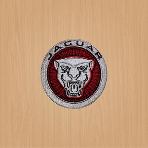 Könnte beinhalten: Ein gestickter silberner und roter Aufnäher mit dem Wort "JAGUAR" in einem Kreis um einen weißen Jaguar-Kopf mit rotem Maul.