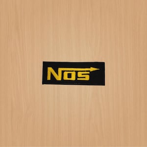 May include: Black and yellow embroidered patch with the word "NOS" and an arrow pointing to the right.