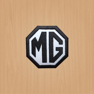 May include: Black and white embroidered patch with the letters MG in a white octagon shape.