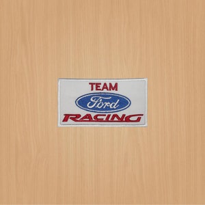 Può includere: Toppa ricamata bianca con le parole "TEAM FORD RACING" in lettere rosse e blu. Il logo Ford è un ovale blu con la parola "Ford" in lettere bianche.