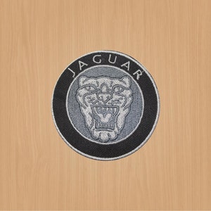 Könnte beinhalten: Ein gestickter schwarzer und silberner Aufnäher mit dem Wort "JAGUAR" in einem Kreis um einen silbernen Jaguar-Kopf.