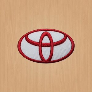 Könnte beinhalten: Gesticktes Toyota-Logo-Patch. Der Patch zeigt das Toyota-Emblem in Rot und Weiß mit einem roten ovalen Rand. Das Logo ist auf einem hellbeige Hintergrund zentriert.