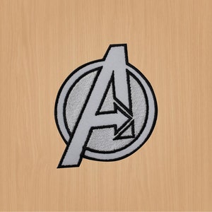 May include: A silver and black embroidered patch featuring the Avengers logo, a stylized letter "A" inside a circle.