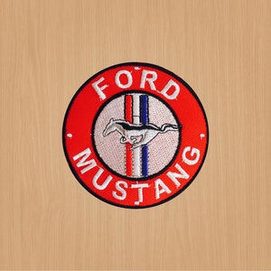 May include: A circular patch with the Ford Mustang logo. The patch has a red outer ring with the words "FORD MUSTANG" in white. Inside, a white circle contains a running silver horse with black details, and red, white, and blue vertical stripes.