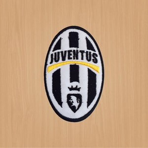 Puede incluir: Parche bordado con el logotipo de la Juventus. El parche ovalado tiene rayas verticales blancas y negras. La palabra "JUVENTUS" está bordada en blanco en la parte superior, con una línea de acento amarilla. Un escudo en la parte inferior.