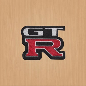 Op de afbeelding: Zwarte en witte geborduurde patch met de tekst "GT-R" in rode en witte letters.