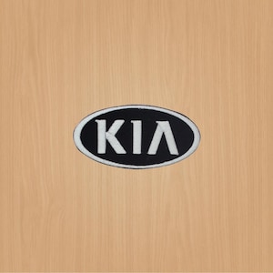 Puede incluir: Un parche ovalado negro con la palabra "KIA" en letras blancas.