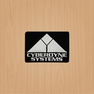 Peut inclure: Un écusson brodé noir et blanc avec le texte "CYBERDYNE SYSTEMS" et un logo triangulaire blanc stylisé.
