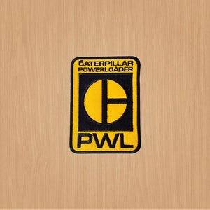 May include: Yellow and black embroidered patch with the text "Caterpillar Powerloader" and the logo "PWL" in a black circle with a yellow cross.