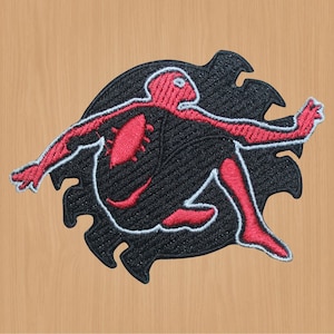 Peut inclure: Patch brodé rouge et noir représentant une silhouette humaine stylisée avec un contour irrégulier. La silhouette est en position de course, les bras tendus.