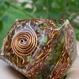 May include: A green and copper crystal grid with a copper wire spiral in the center. The grid is made of clear resin and has a geometric shape.