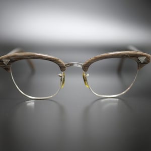 May include: Eyeglasses with a retro design. The frames feature a combination of brown wood-grain upper rims and silver-colored lower rims. Small silver triangle details are on the corners of the upper rims. The lenses are clear.